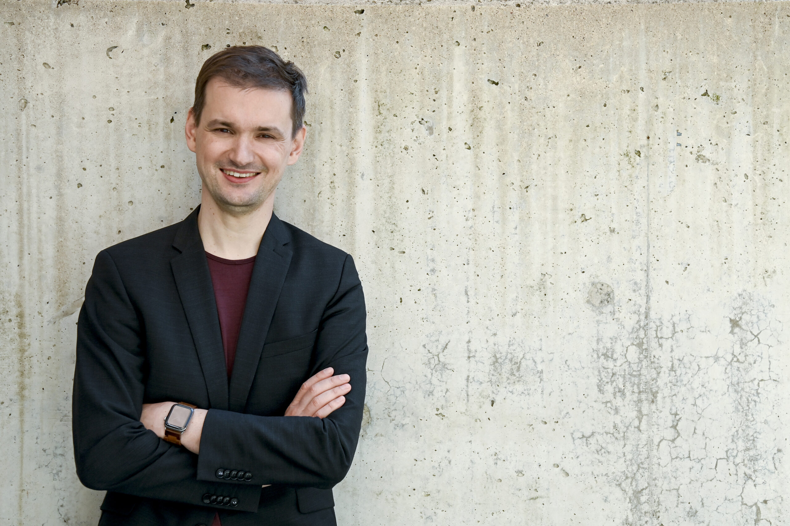 Dominic verschränkt die Arme und lehnt an einer Wand.